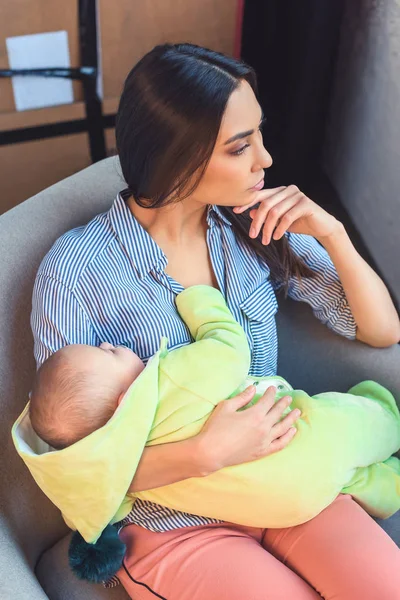 Mãe pensativa com bebê infantil descansando na cadeira de braço em casa — Fotografia de Stock