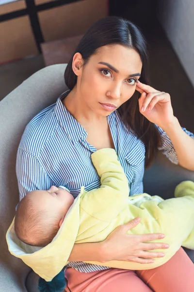 Портрет задумчивой матери с младенцем, отдыхающим на кресле дома — стоковое фото