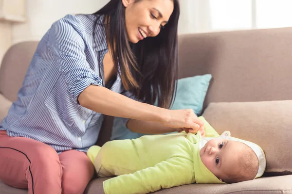 Smiling mother dressing infant baby up at home — Stock Photo