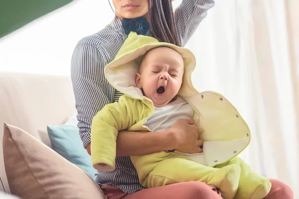 Обрізаний знімок мами, що тримає позіхання дитини на руках вдома — стокове фото
