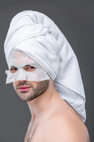 Bel homme avec serviette et masque de collagène, isolé sur gris, concept de soins de la peau — Photo de stock