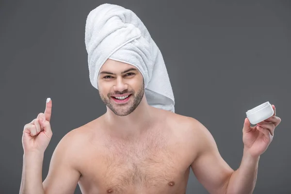 Cheerful beardman in towel holding face cream, isolated on grey — Stock Photo