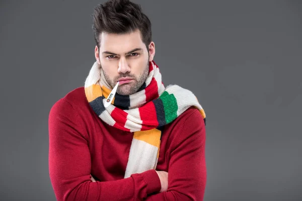 Ill man with thermometer in warm scarf, isolated on grey — Stock Photo