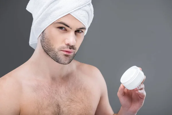 Bearded man in towel holding face cream, isolated on grey — Stock Photo