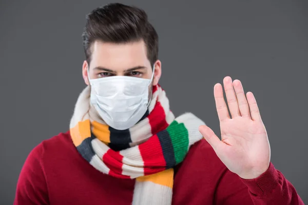 Sick man in warm scarf and medical mask with stop sign, isolated on grey — Stock Photo