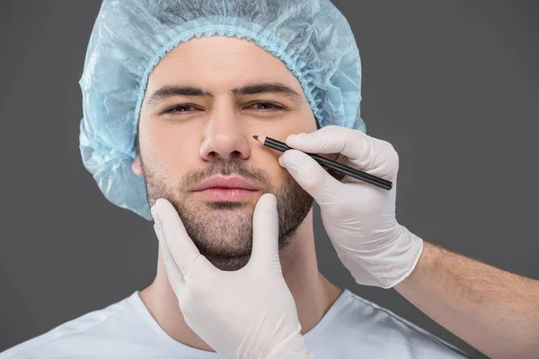 Arzt zeichnet Linien für Facelifting an gutaussehendem Mann, isoliert auf grau — Stockfoto