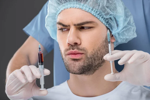 Bel homme en bonnet médical choisissant des injections de beauté, isolé sur gris — Photo de stock