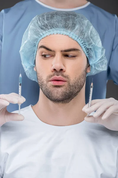 Homem bonito barbudo em tampa médica escolhendo injeções de beleza, isolado em cinza — Fotografia de Stock