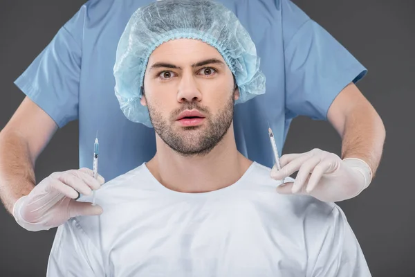Homem bonito chocado em boné médico fazendo injeções de beleza, isolado em cinza — Fotografia de Stock
