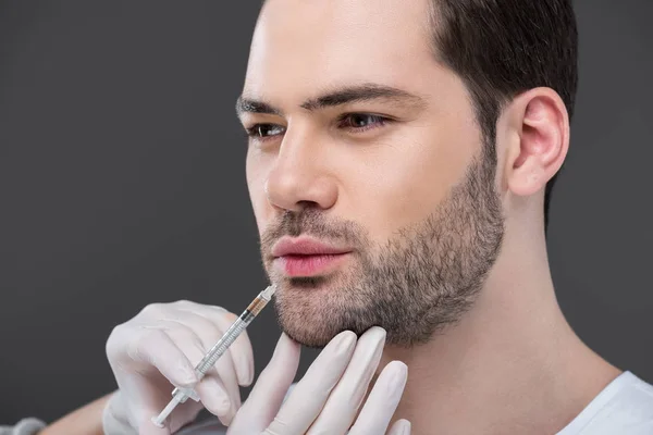 Mãos em luvas médicas fazendo injeção de beleza para homem barbudo, isolado em cinza — Fotografia de Stock
