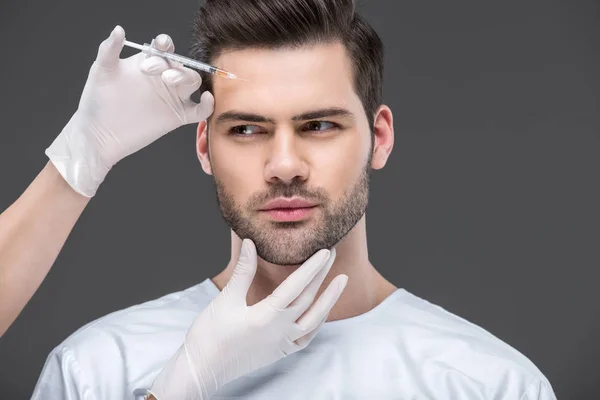 Manos en guantes médicos haciendo inyección de belleza para hombre guapo, aislado en gris — Stock Photo