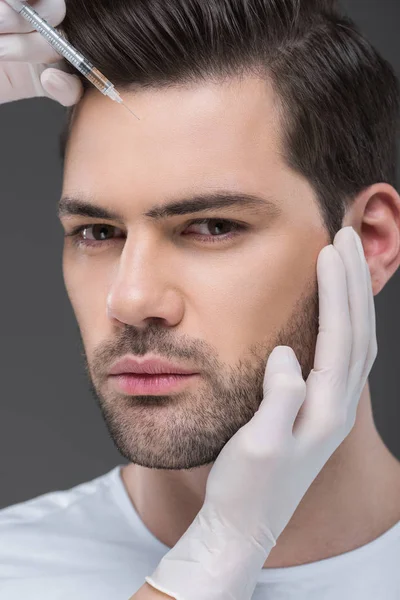 Manos en guantes médicos haciendo inyección de belleza para hombre guapo, aislado en gris - foto de stock