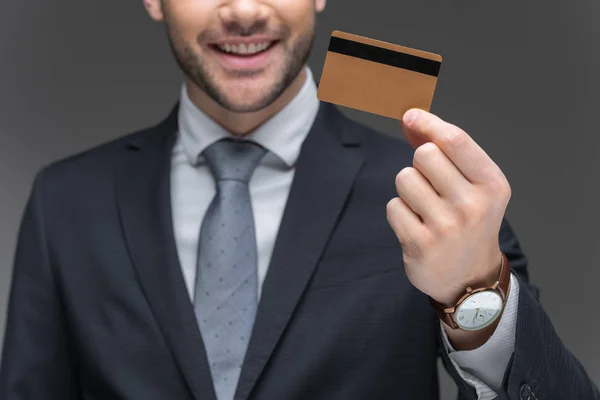 Vista ritagliata di uomo d'affari in possesso di carta di credito dorata, isolato su grigio — Foto stock