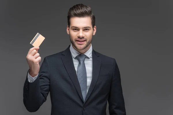 Allegro uomo d'affari in possesso di carta di credito, isolato su grigio — Foto stock