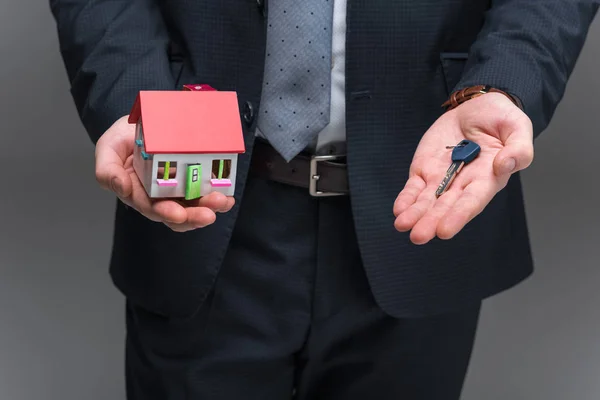 Cropped view of realtor holding house model and key, isolated on grey — Stock Photo