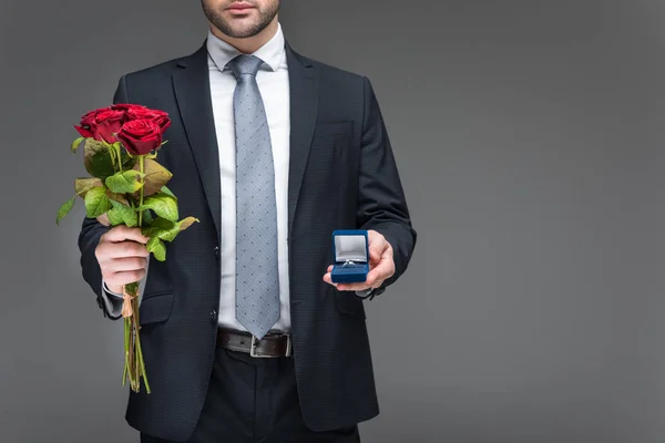 Cropped view of man holding bouquet of red roses and proposal ring, isolated on grey — Stock Photo