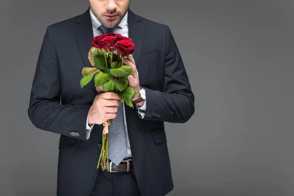 Vista recortada del hombre sosteniendo ramo de rosas rojas, aislado en gris — Stock Photo