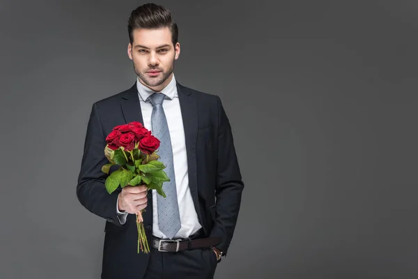 Handsome man holding bouquet of red roses, isolated on grey — Stock Photo