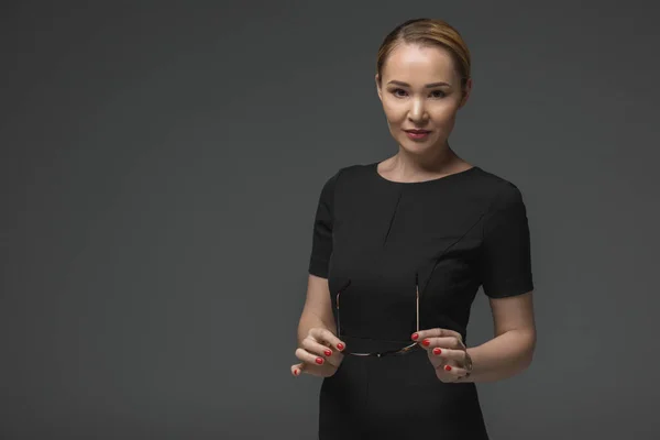 Beautiful kazakh woman holding eyeglases and looking at camera isolated on grey — Stock Photo