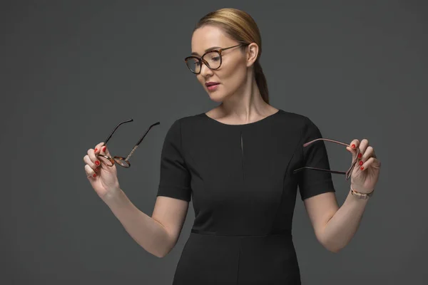 Hermosa mujer kazakh en vestido negro elegir gafas aisladas en gris - foto de stock