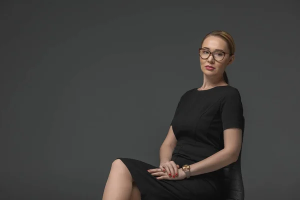 Belle femme kazakh dans les lunettes assis sur la chaise et regardant la caméra isolée sur gris — Photo de stock