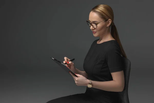 Hermosa mujer de negocios kazakh escribir en portapapeles en gris - foto de stock