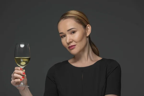 Mujer kazakh sonriente sosteniendo un vaso de vino y mirando a la cámara aislada en gris - foto de stock