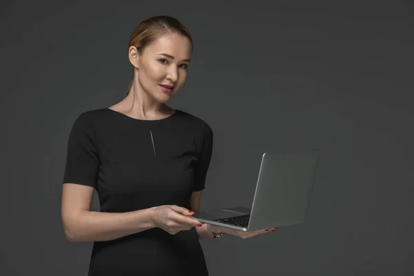 Schöne kasachische Frau hält Laptop in der Hand und lächelt in die Kamera isoliert auf grau — Stockfoto