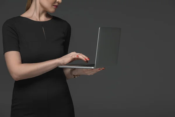 Cropped shot of woman in black dress using laptop isolated on grey — Stock Photo