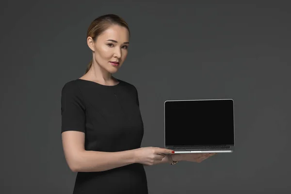 Bela mulher kazakh segurando laptop com tela em branco e olhando para a câmera isolada no cinza — Fotografia de Stock