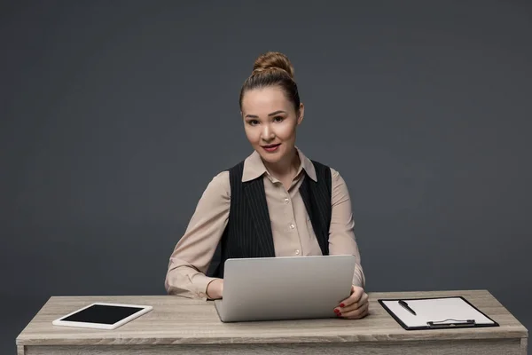 Belle femme d'affaires kazakh utilisant un ordinateur portable et souriant à la caméra isolée sur gris — Photo de stock