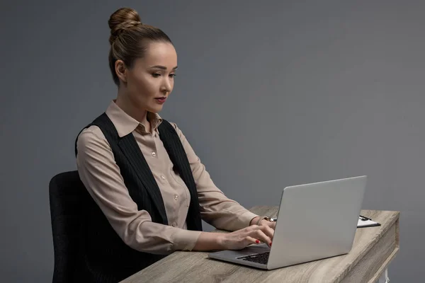 Hermosa mujer de negocios kazakh utilizando el ordenador portátil en la mesa aislado en gris - foto de stock