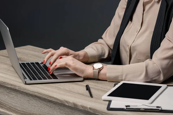 Cropped shot of businesswoman using laptop at table on grey — Stock Photo