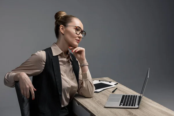 Pensativa mujer de negocios kazakh en gafas usando portátil aislado en gris - foto de stock