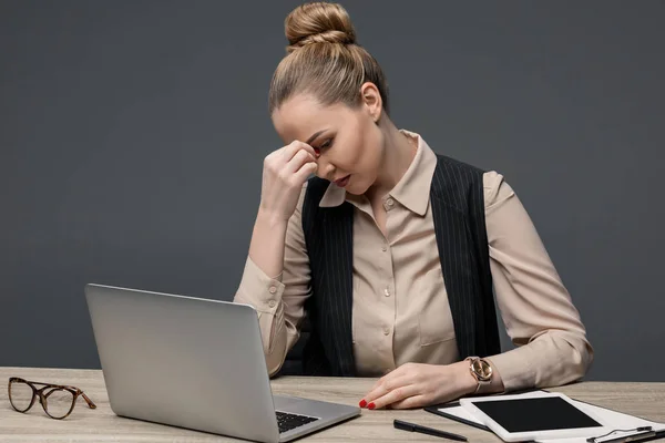 Müde kasachische Geschäftsfrau mit Laptop am Tisch isoliert auf grau — Stockfoto