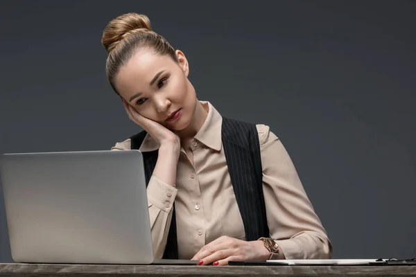 Tired kazakh businesswoman using laptop at table isolated on grey — Stock Photo