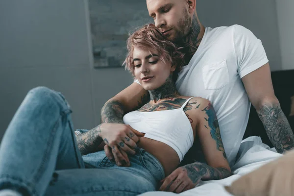 Tender tattooed couple hugging, holding hands and lying on bed — Stock Photo