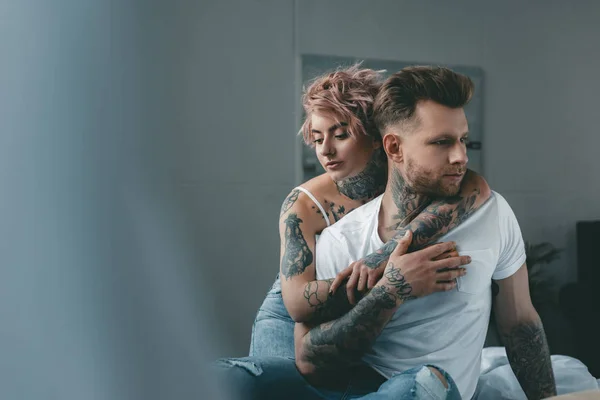 Tattooed girl hugging her boyfriend on bed in bedroom — Stock Photo