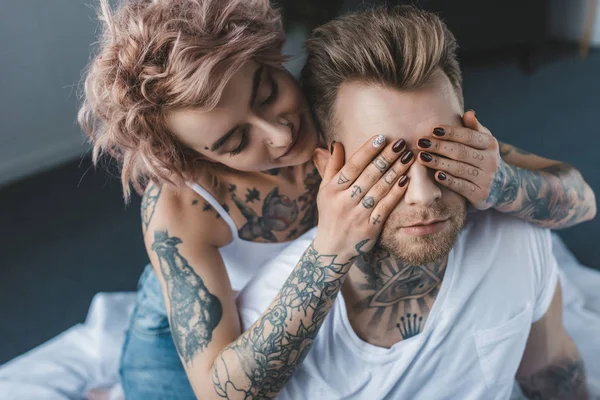 Belle fille tatouée fermer les yeux de son petit ami — Photo de stock