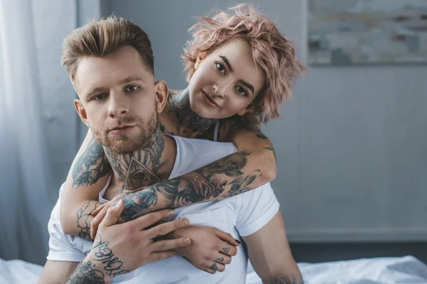 Smiling tattooed girl hugging her boyfriend on bed in bedroom — Stock Photo