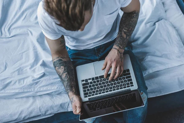 Vista aerea dell'uomo tatuato che utilizza il computer portatile a letto — Foto stock