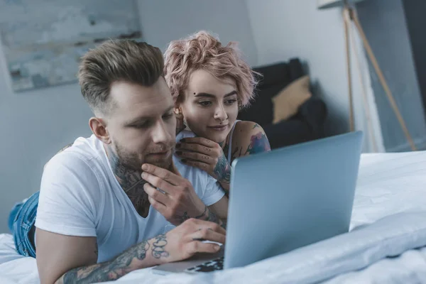 Hermosa pareja tatuada usando portátil en la cama - foto de stock