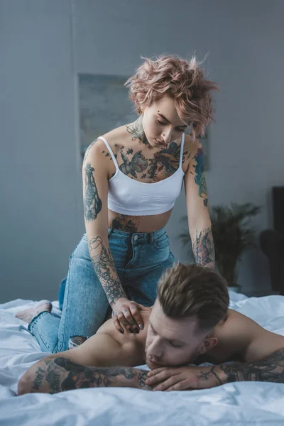 Hermosa novia tatuada haciendo masaje para su novio en la cama - foto de stock