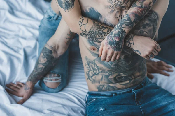 Cropped view of girlfriend embracing her tattooed boyfriend in bed — Stock Photo