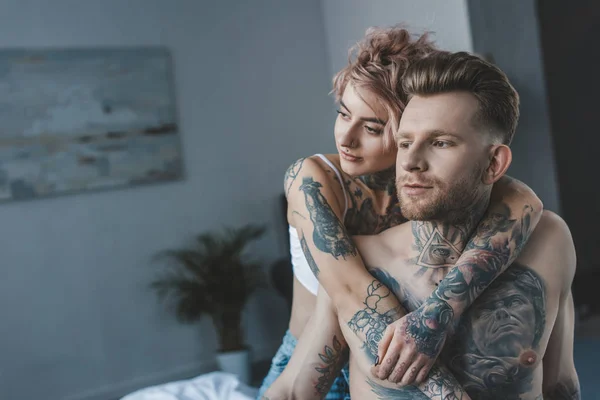 Joven novia abrazando su tatuado novio en la cama - foto de stock