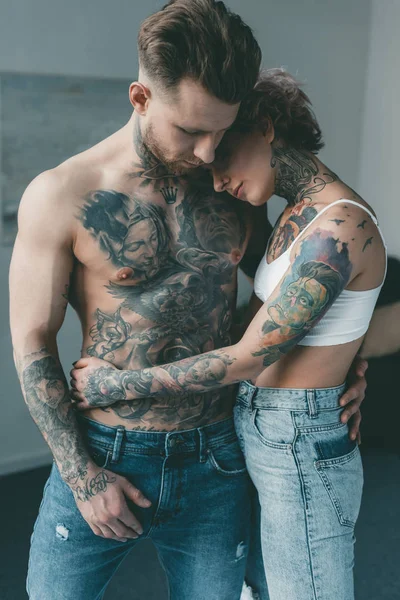 Elegantes amantes tatuados abrazándose en el dormitorio - foto de stock