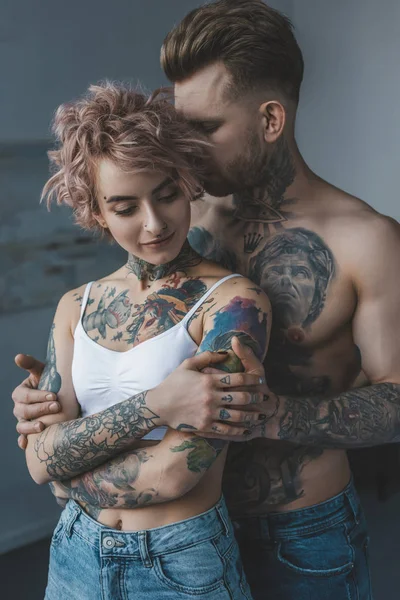 Concurso casal tatuado abraçando no quarto em casa — Fotografia de Stock