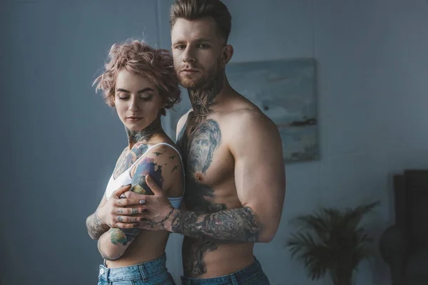 Jovem tatuado casal abraçando no quarto — Fotografia de Stock