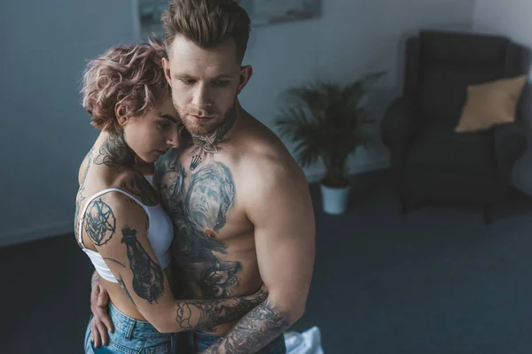 Tierna pareja tatuada abrazándose en el dormitorio - foto de stock