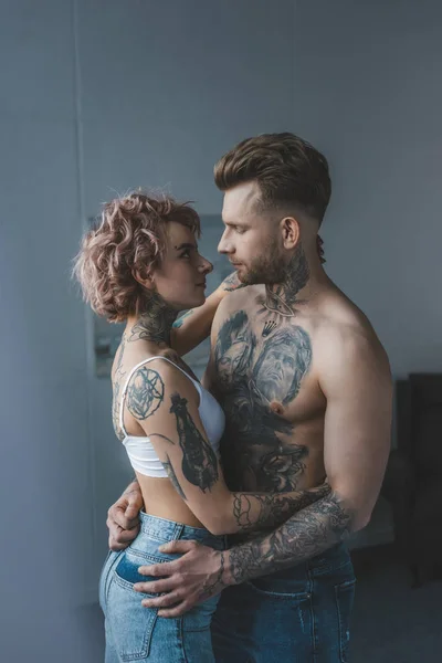 Joven pareja tatuada abrazándose en el dormitorio - foto de stock